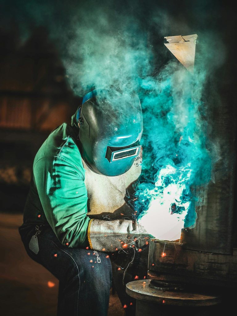 A skilled worker welds metal indoors, producing bright sparks and vivid colors.