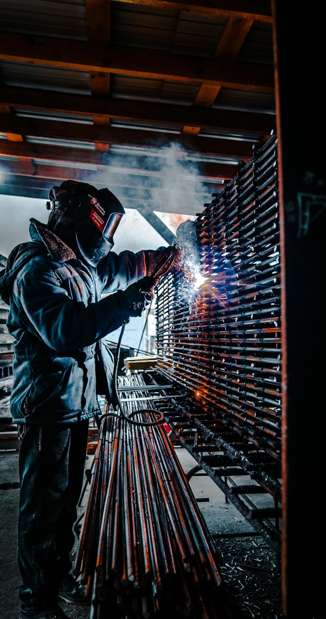 A welder uses a torch to spark and fuse metal rods indoors, capturing the vibrant energy of industrial work.