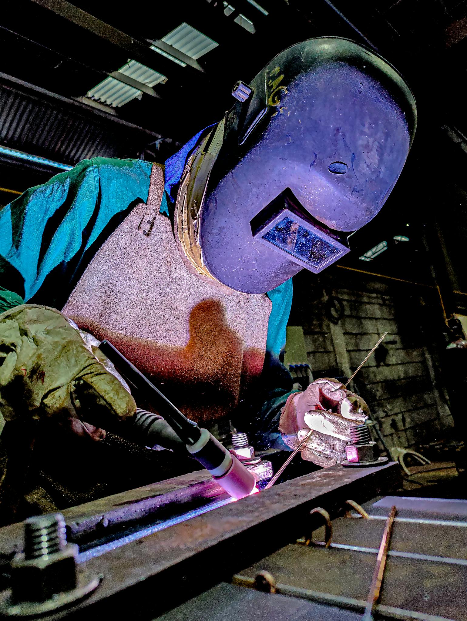 Skilled welder wearing protective gear engages in precise welding in a factory environment.